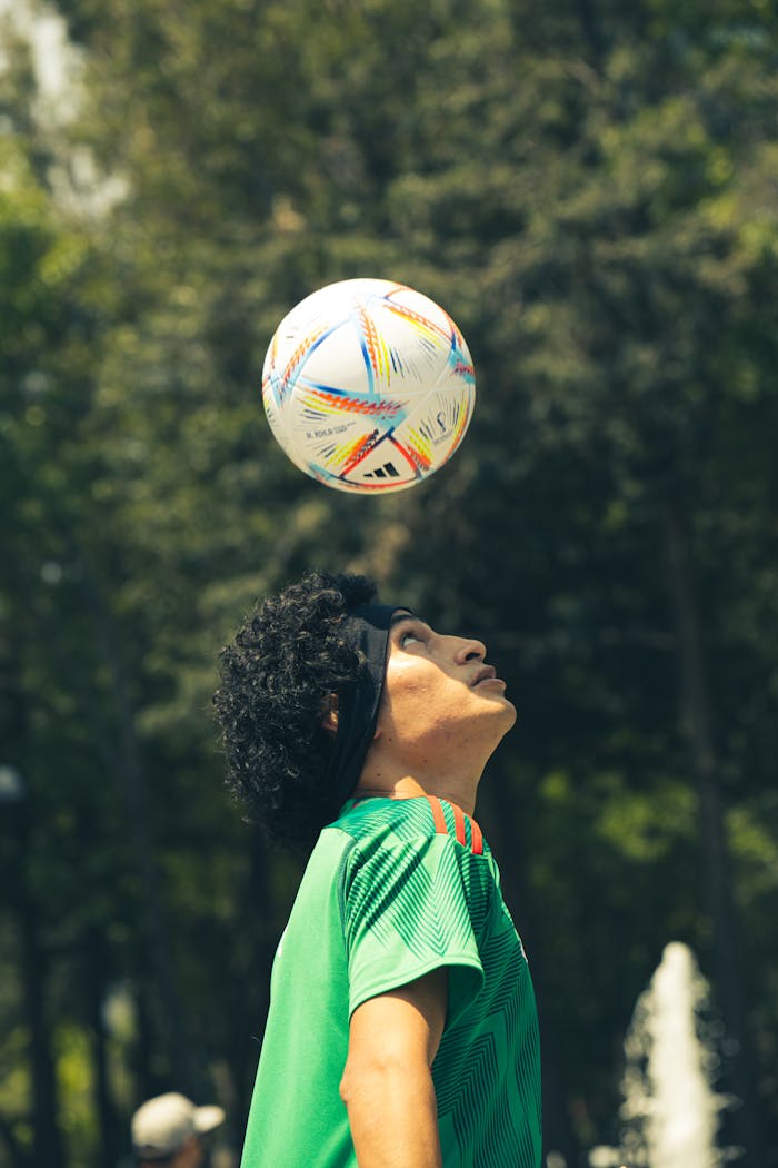 A young footballer demonstrates a heading skill with focus, showcasing ball control against a natural backdrop.